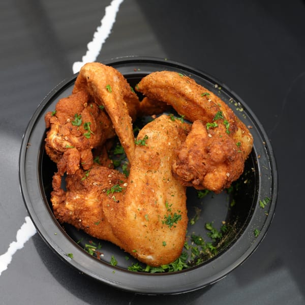 Crispy fried chicken wings, seasoned with herbs and spices, in a black bowl on a dark counter.