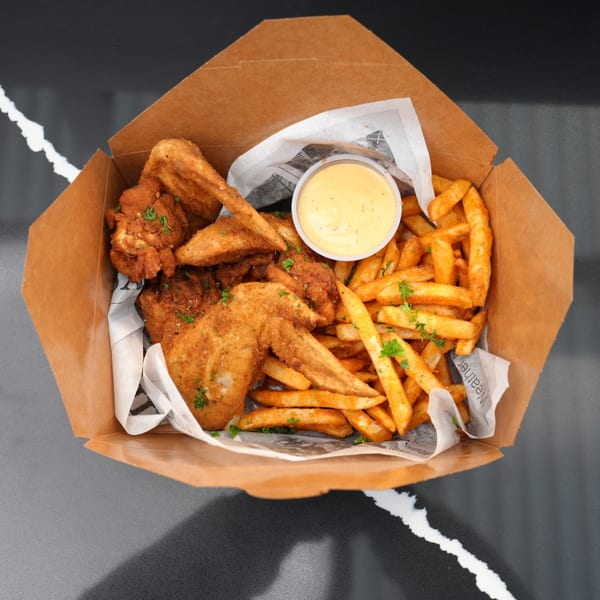 Crispy fried chicken wings and golden french fries with a side of dipping sauce in a takeout box.