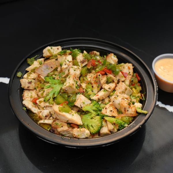 Chicken and broccoli stir-fry with red peppers and onions in a black bowl, with a side of sauce.
