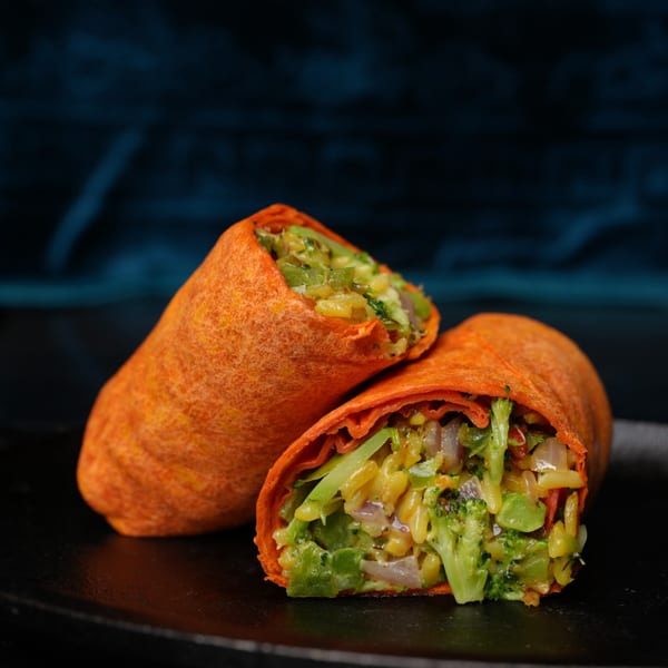 Two vibrant orange wraps, one cut in half, revealing a colorful filling of broccoli, rice, and vegetables.