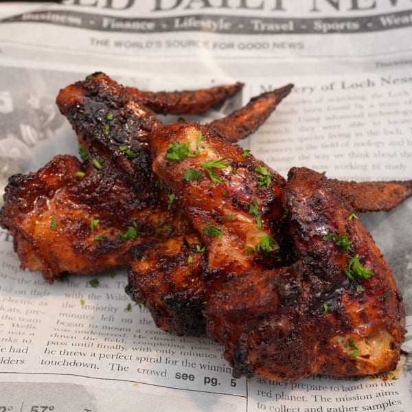Close-up of several glazed chicken wings with parsley on newspaper.