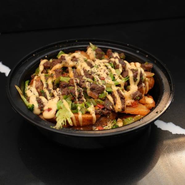 A black bowl filled with steak, broccoli, and fries, drizzled with a creamy sauce.