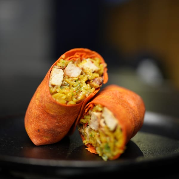 Two halves of a chicken and rice burrito with an orange tortilla, on a dark plate.