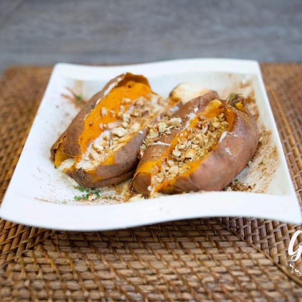 Two baked sweet potatoes, halved and filled with orange mash, cream, and chopped nuts, on a white plate.
